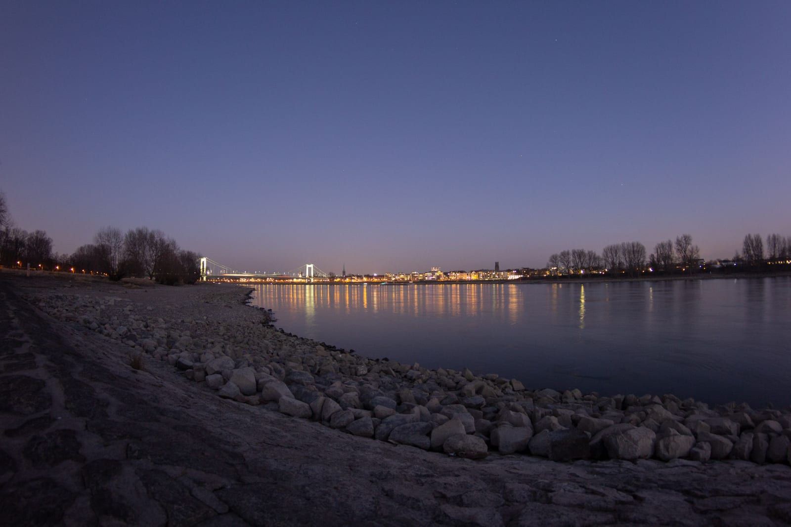 Rheinufer in der Abenddämmerung mit Lichtern der Stadt am anderen Ufer