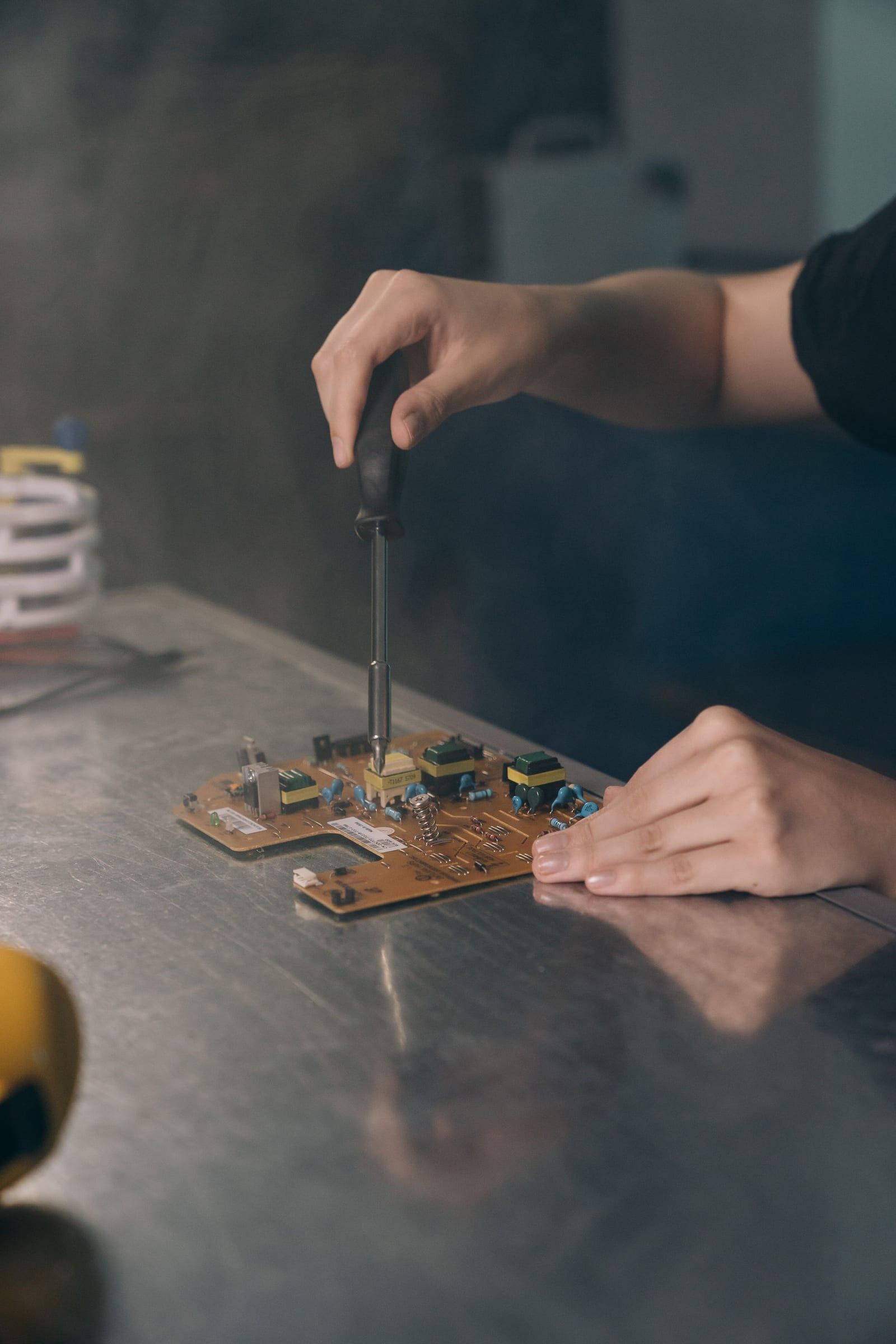 Hände prüfen mit einem Schraubendreher eine Platine